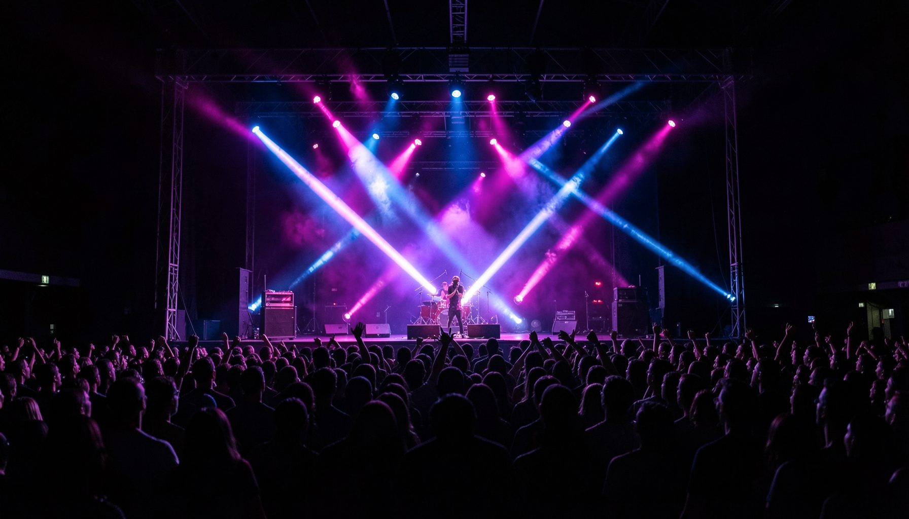 Palco de show visto de longe com luzes roxas e azuis cruzando o ar, plateia em silhueta, atmosfera de concerto ao vivo